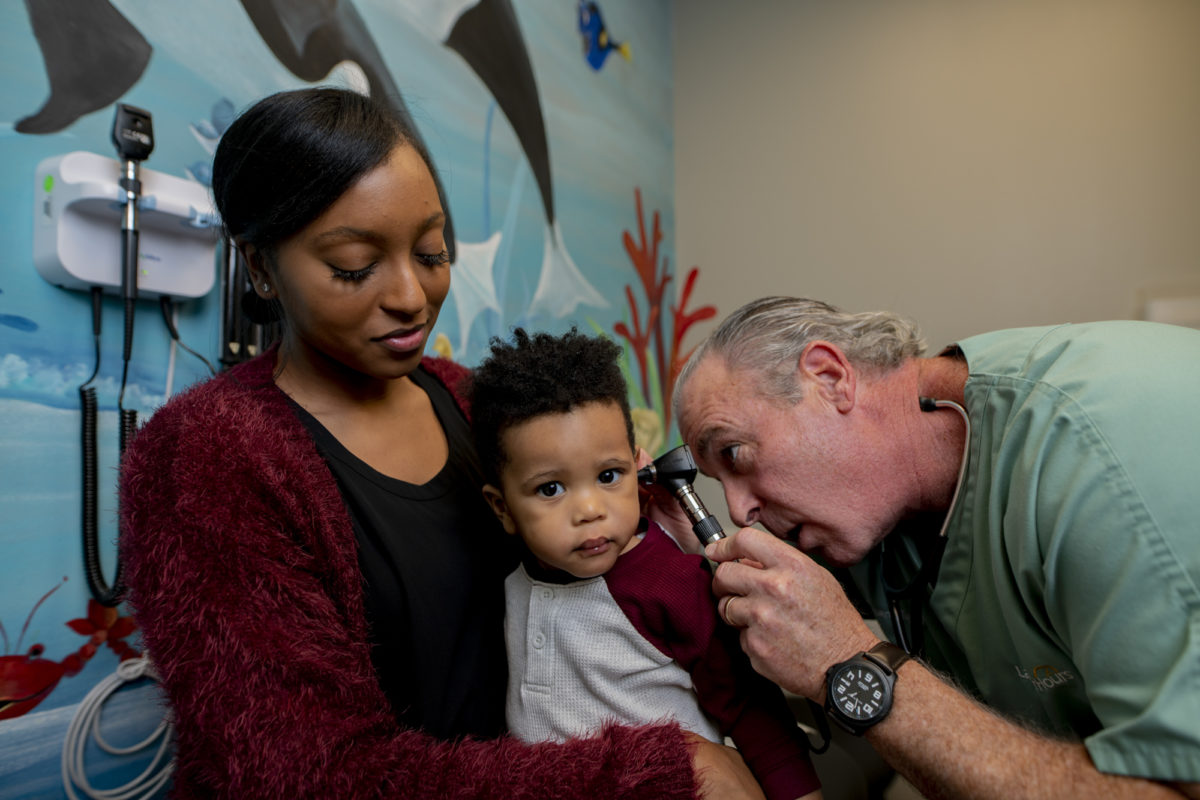 A young boy being held by his mother as he gets an ear exam.