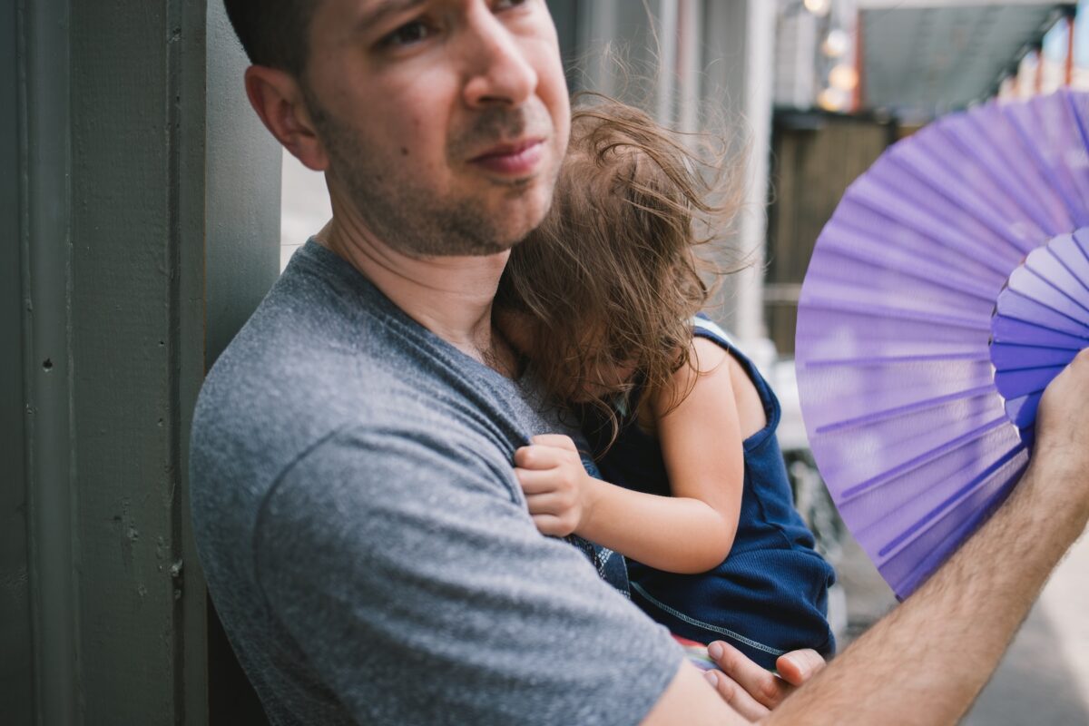Man holds toddler and fans her on hot summer day