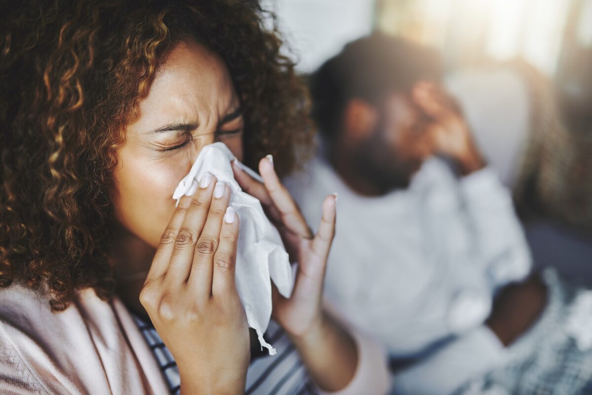 Young woman and husband sneezing, showing signs of sickness